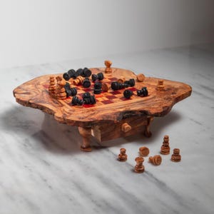 May include: A wooden chess set with a live edge design. The chess board has a red and brown checkered pattern. Black and brown chess pieces are scattered across the board and some are placed on the side. The chess set is on a white marble surface.