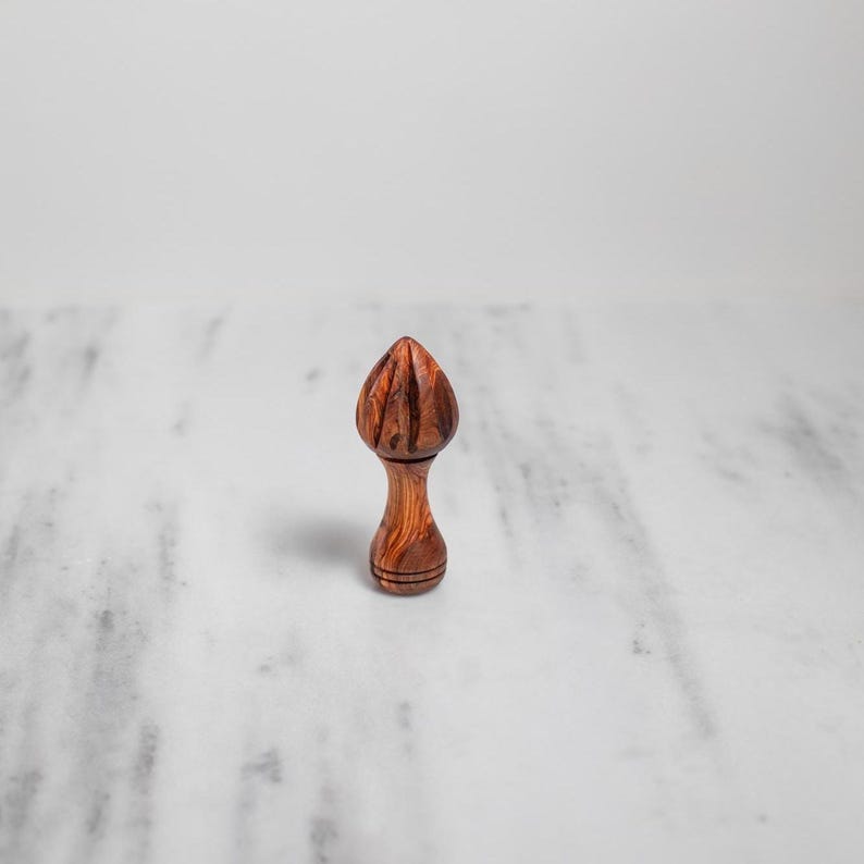 May include: A wooden citrus reamer with a bulbous, ridged top and a slender, rounded handle. The reamer is made of a dark, reddish-brown wood with visible grain patterns. It is designed for juicing citrus fruits.