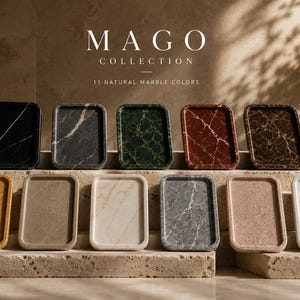 May include: Eleven rectangular marble trays from the Mago Collection displayed in two rows. The trays feature various natural stone colors including black, dark gray, green, red, brown, gold, tan, beige, light gray, pink, and white with veining.