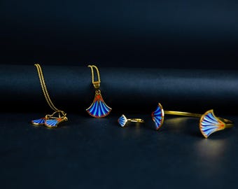 May include: A gold jewelry set consisting of a necklace with a fan-shaped pendant, a pair of matching earrings, a ring, and an open cuff bracelet. Each piece features a vibrant enamel inlay with blue, white, and orange stripes in a fan pattern.