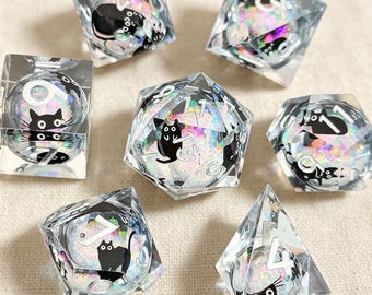 May include: A set of seven polyhedral dice made of clear resin, each containing iridescent glitter and small black cat illustrations. The numbers are printed in white, and the set includes various geometric shapes such as cubes and pyramids.