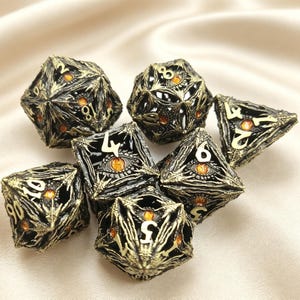May include: A set of seven polyhedral dice featuring an intricate, dark metallic finish with raised, textured skeletal patterns. Each die face incorporates a detailed, realistic orange eye design with a black pupil, complemented by bold, light-colored numerals.