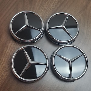May include: Four black and silver Mercedes-Benz wheel center caps. Each cap features the iconic three-pointed star emblem in silver against a glossy black background, surrounded by a silver ring.