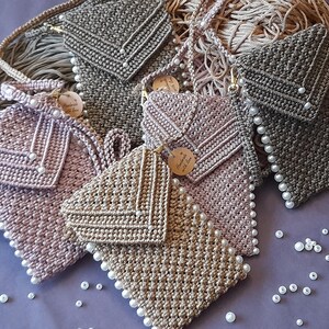 以下が含まれることがあります： パールがあしらわれたクロシェバッグが4つ。バッグは茶色、ピンク、グレーの色合いです。バッグはすべて小さく、フラップで閉じられます。バッグは紫色の表面に置かれ、周りに白いパールが散らばっています。