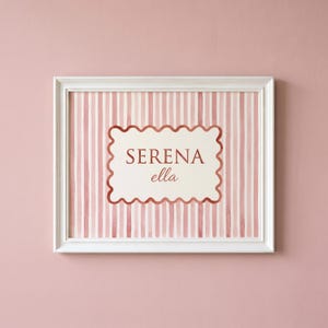 May include: A white-framed wall art print featuring a vertical pink and white striped background. In the center, a cream-colored scalloped rectangle contains the text SERENA in uppercase letters and the name ella in a cursive script font.