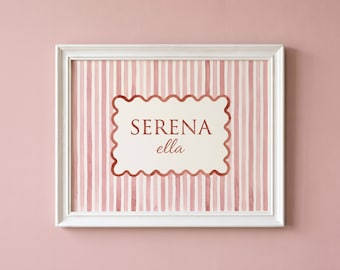 May include: A white-framed wall art print featuring a vertical pink and white striped background. In the centre, a cream-coloured scalloped rectangle contains the text SERENA in uppercase letters and the name ella in a cursive script font.