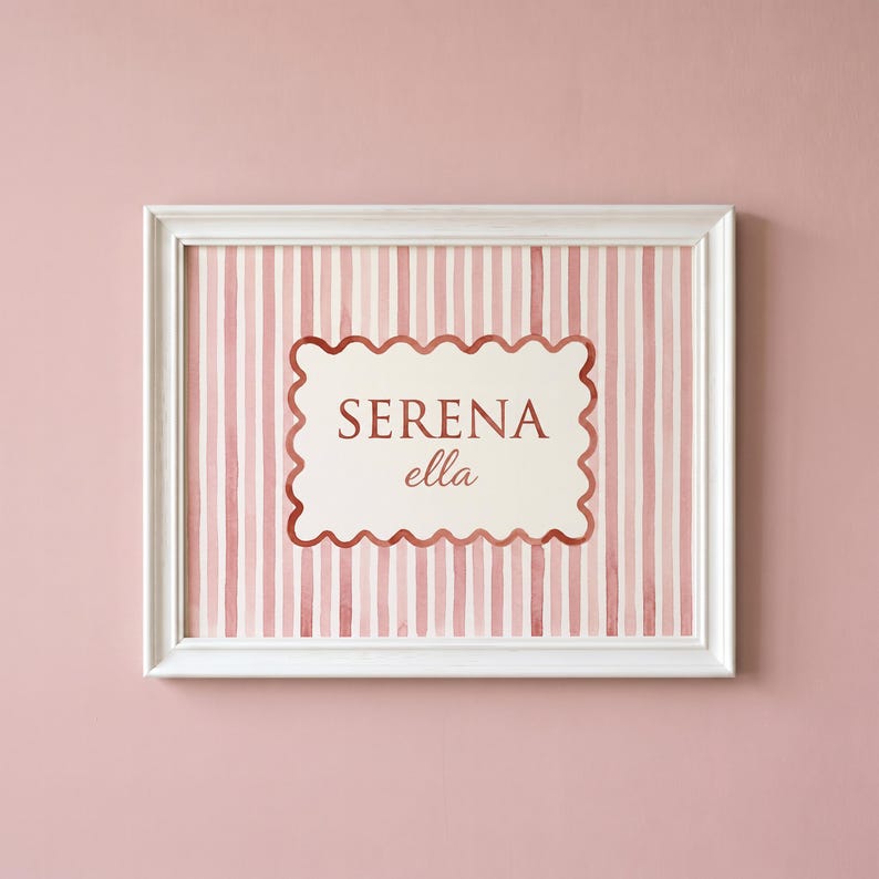 May include: A white-framed wall art print featuring a vertical pink and white striped background. In the center, a cream-colored scalloped rectangle contains the text SERENA in uppercase letters and the name ella in a cursive script font.
