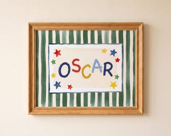 May include: A framed print featuring the name OSCAR in multicolored hand-painted style letters on a cream background. The name is surrounded by small red, blue, yellow, and green stars, all set against a dark green and white vertical striped backdrop.