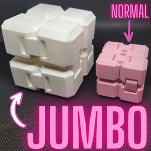 May include: Two fidget cubes, one white and one pink, are shown side-by-side. The white cube is labeled "JUMBO" and the pink cube is labeled "NORMAL".