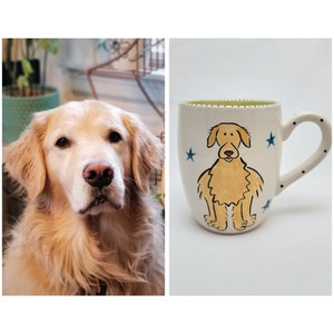 May include: A white ceramic mug with a hand-painted illustration of a golden retriever dog. The dog is sitting with its paws together and has a happy expression. The mug has a green rim and a black handle with white polka dots.
