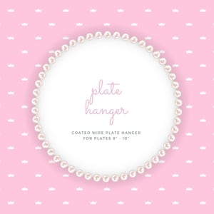 May include: A white pearl-like wire plate hanger with the text "plate hanger" and "COATED WIRE PLATE HANGER FOR PLATES 8" - 10" ". The hanger is on a pink background with a white crown pattern.