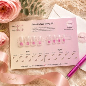 Op de afbeelding: Een set voor het opmeten van nagels op een rechthoekige kaart met een kleurverloop. De kaart bevat doorzichtige plastic nageltips met roze cijfers, instructies en secties om de maten voor de linker- en rechterhand te noteren.