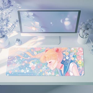 Op de afbeelding: Een rechthoekige muismat met een pastelkleurige anime-illustratie. Het toont een personage met blond haar en een matrozenuniform, tegen een bloemrijke en dromerige achtergrond in roze, blauw en wit.