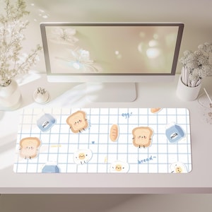 May include: A rectangular desk mat featuring a white grid pattern on a light blue background. The design includes repeating cartoon illustrations of smiling toast slices, fried eggs, and blue milk cartons, with the text egg and bread written in blue.