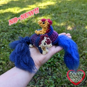 May include: Two crocheted creatures with blue, purple, red, and yellow accents. One creature is atop the other. The image includes the text "NO-SEW!!" and "MAY 2026". The creatures have blue tails.