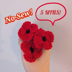May include: Hand holding three red crocheted poppy flowers with black centers. Text in the image reads "No-Sew!" and "5 MINS!" in a red speech bubble. The poppies are handmade and likely for crafting or decoration.