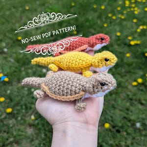 Peut inclure: Trois figurines de reptiles crochetées en nuances de marron, jaune et orange sont empilées. Le texte "NO-SEW PDF PATTERN!" est affiché au-dessus des figurines. Les figurines sont tenues dans une main sur un fond vert.