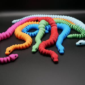 May include: A set of colourful, segmented, flexible snake toys. The snakes are made of a soft, rubbery material and are in various colours, including pink, orange, green, blue, and red.