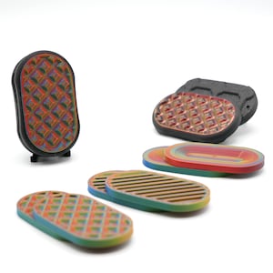 Puede incluir: Una colección de objetos coloridos con patrones geométricos. Los objetos incluyen una pieza negra vertical con una superficie con patrón de diamantes multicolores y varias piezas ovaladas con patrones de rayas y diamantes en varios colores.