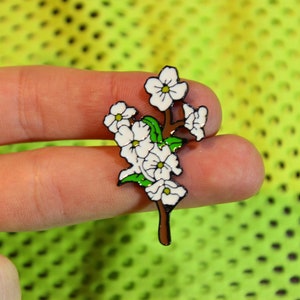 May include: White enamel flower pin with green leaves and a brown stem. The pin is a cluster of five flowers.