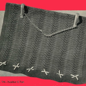 May include: A gray knitted blanket with a feather and fan stitch pattern. The blanket has a fringe border and is decorated with white bows. The text "No. 514 - Feather & Fan" is printed at the bottom of the image.