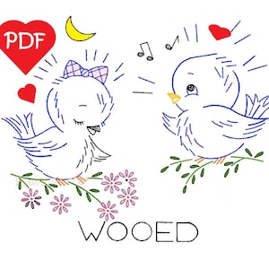 Könnte beinhalten: Ein digitales Stickmuster mit zwei blauen Vögeln, über denen sich ein Herz und Noten befinden. Der Text "WOQED" befindet sich unter den Vögeln. Das Muster ist als PDF-Download verfügbar.