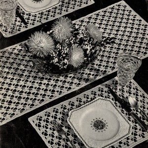 Puede incluir: Tres manteles individuales de crochet blanco con un delicado diseño calado. Los manteles individuales están colocados sobre una superficie oscura con un plato blanco y cubiertos en cada uno. Un ramo de flores blancas está en el centro de la mesa.