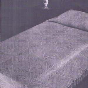 May include: A crocheted throw blanket with a geometric pattern and fringe. The blanket is a light purple color and is draped over a bed.
