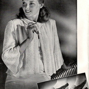 Può includere: Una fotografia in bianco e nero di una donna che indossa un cardigan bianco lavorato a uncinetto con un motivo a pizzo. La donna è seduta su una sedia con le gambe incrociate. La foto mostra anche un paio di pantofole all'uncinetto.