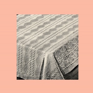 May include: A white knitted blanket with a cable knit pattern and a chevron pattern. The blanket is folded in half and the edges are visible.