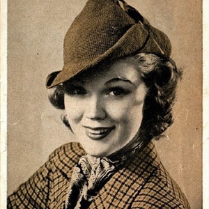May include: A woman wearing a brown and black plaid jacket with a brown felt hat with a feather. The hat is angled to the side and the woman is smiling. The text "The Robin Hood (See page 2)" is at the bottom of the image.