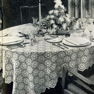 May include: A white crocheted tablecloth with a delicate floral pattern covers a round table set for a formal dinner. The table is decorated with a centerpiece of white flowers and a lit candle.