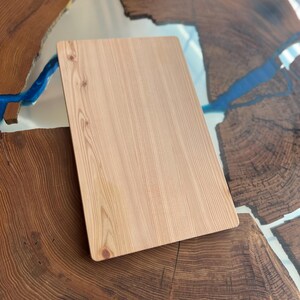 Op de afbeelding: Een lichtbruin houten snijplank met een glad oppervlak en een licht afgeronde rand. De plank ligt op een tafel met een ontwerp van blauw en bruin epoxyhars.