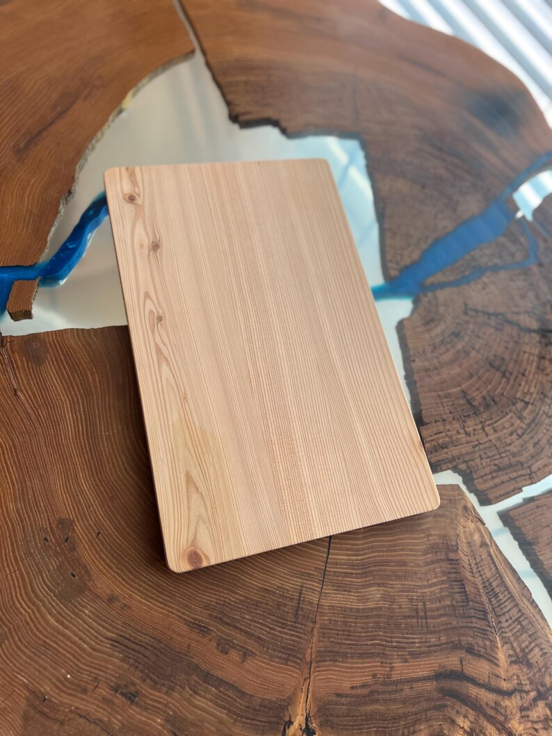 Op de afbeelding: Een lichtbruin houten snijplank met een glad oppervlak en een licht afgeronde rand. De plank ligt op een tafel met een ontwerp van blauw en bruin epoxyhars.