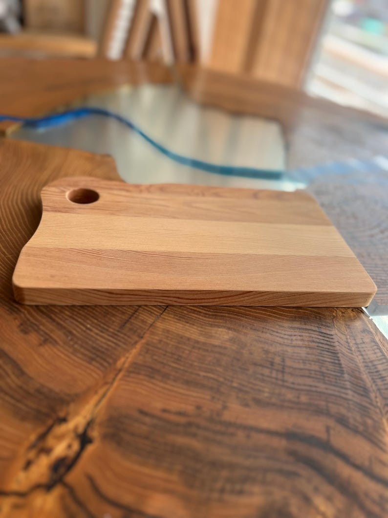 May include: A rectangular wooden cutting board with a small hole in the top. The board has a light brown color and a smooth surface.