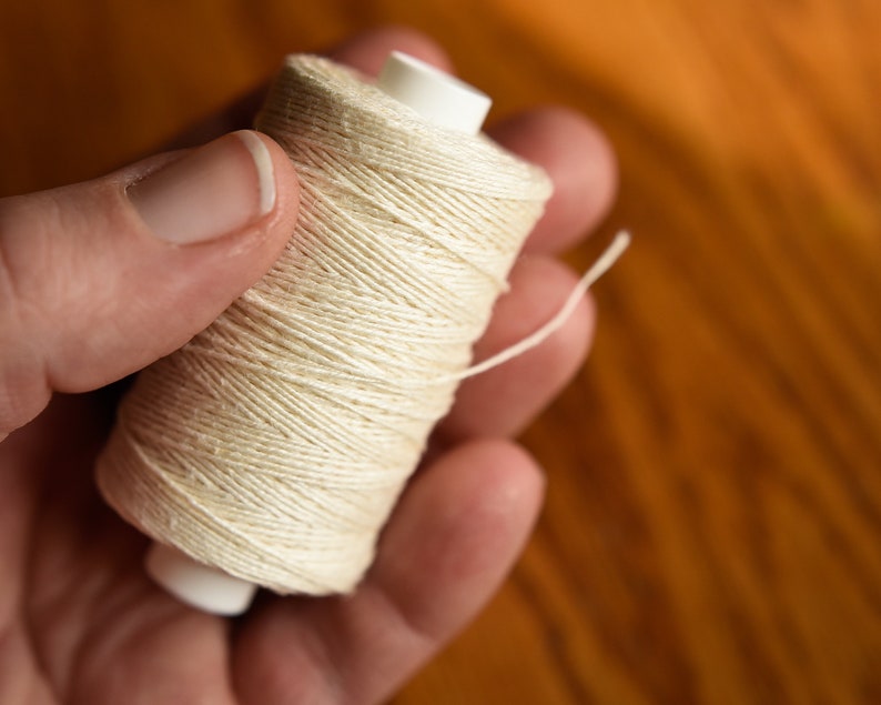 Puede incluir: Una bobina de hilo blanco con una bobina de pl&aacute;stico blanco.