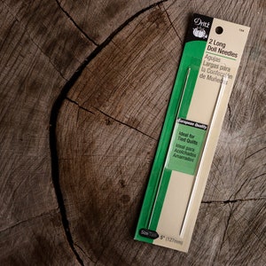 May include: A package of two long doll needles, 5 inches in length, ideal for tied quilts. The package is white with green accents and features the text "Dritz 2 Long Doll Needles" and "Ideal for Tied Quilts".