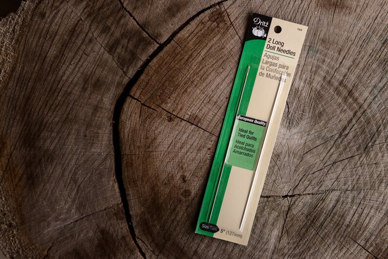 May include: A package of two long doll needles, 5 inches in length, ideal for tied quilts. The package is white with green accents and features the text "Dritz 2 Long Doll Needles" and "Ideal for Tied Quilts".