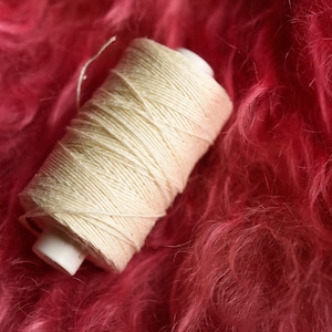 Puede incluir: Una bobina de hilo blanco sobre una superficie rosa y peluda.