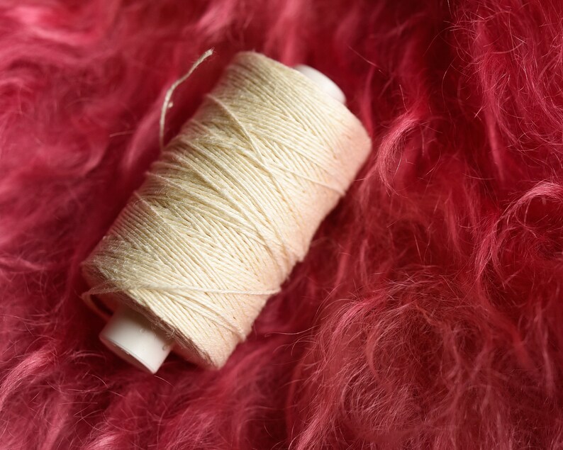 Puede incluir: Una bobina de hilo blanco sobre una superficie rosa y peluda.