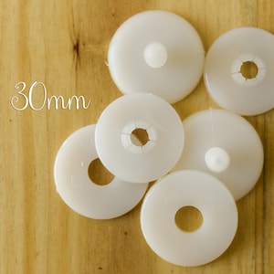 K&ouml;nnte beinhalten: Sechs wei&szlig;e runde M&ouml;belkappen aus Kunststoff mit einem Durchmesser von 30 mm, einem Loch in der Mitte und einem kleinen, erhabenen Knopf in der Mitte.