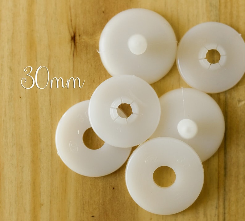 K&ouml;nnte beinhalten: Sechs wei&szlig;e runde M&ouml;belkappen aus Kunststoff mit einem Durchmesser von 30 mm, einem Loch in der Mitte und einem kleinen, erhabenen Knopf in der Mitte.