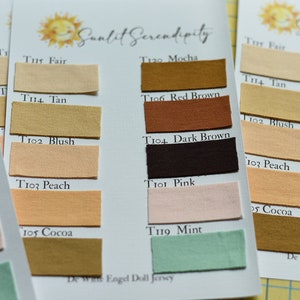 Op de afbeelding: Close-up van stofkleurstalen met namen als "Fair", "Tan", "Blush" en "Peach". De stalen zijn gerangschikt op witte kaarten met het "Sunlit Serendipity" logo. De stofkleuren vari&euml;ren van lichtbeige tot donkerbruin.