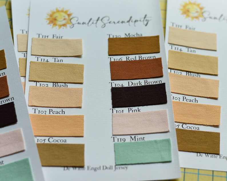 Op de afbeelding: Close-up van stofkleurstalen met namen als "Fair", "Tan", "Blush" en "Peach". De stalen zijn gerangschikt op witte kaarten met het "Sunlit Serendipity" logo. De stofkleuren vari&euml;ren van lichtbeige tot donkerbruin.