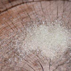 May include: A close-up of a pile of small, clear glass beads on a wooden surface. The beads are round and translucent, and they are scattered randomly across the surface.