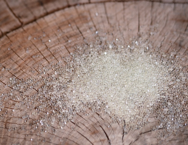 May include: A close-up of a pile of small, clear glass beads on a wooden surface. The beads are round and translucent, and they are scattered randomly across the surface.