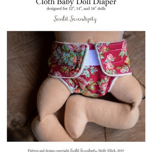 May include: A cloth baby doll diaper with a floral pattern in red, pink, and green. The diaper is designed for 12", 14", and 16" dolls. The text "Cloth Baby Doll Diaper" and "Sunlit Serendipity" are visible.