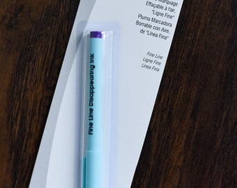 May include: A blue air erasable marking pen with a purple cap. The packaging reads "The Fine Line" Air Erasable Marking Pen, Stylo de Marquage Effaçable à l'air, "Ligne Fine", Pluma Marcadora Borrable con Aire, de "Línea Fina", Fine Line, Ligne Fine, Linea Fina.