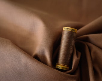 May include: A spool of brown thread with a yellow label that reads "Gutermann" and "100 m - 110 yds" on a brown fabric background.