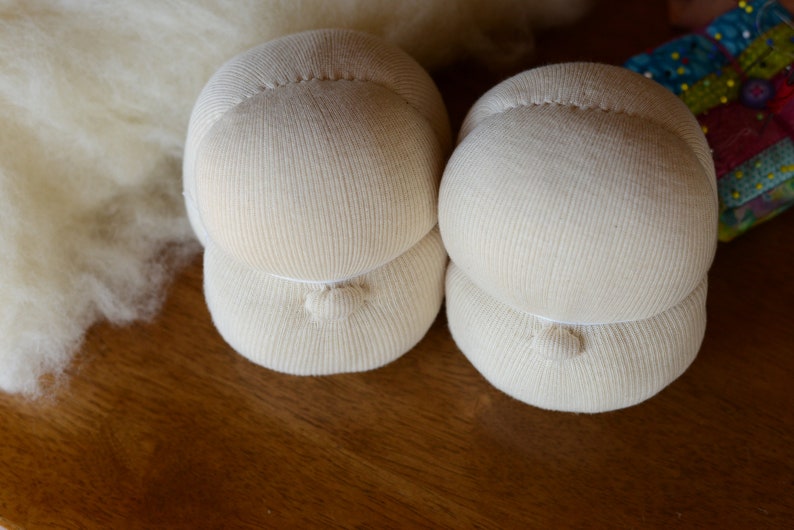 Puede incluir: Dos cabezas de mu&ntilde;eca de tela blanca con una superficie texturizada. Las cabezas est&aacute;n apiladas una encima de la otra.